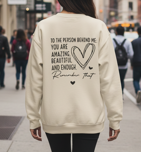 Woman wearing a sweatshirt walking down the street with the quote "to the person behind me you are amazing"